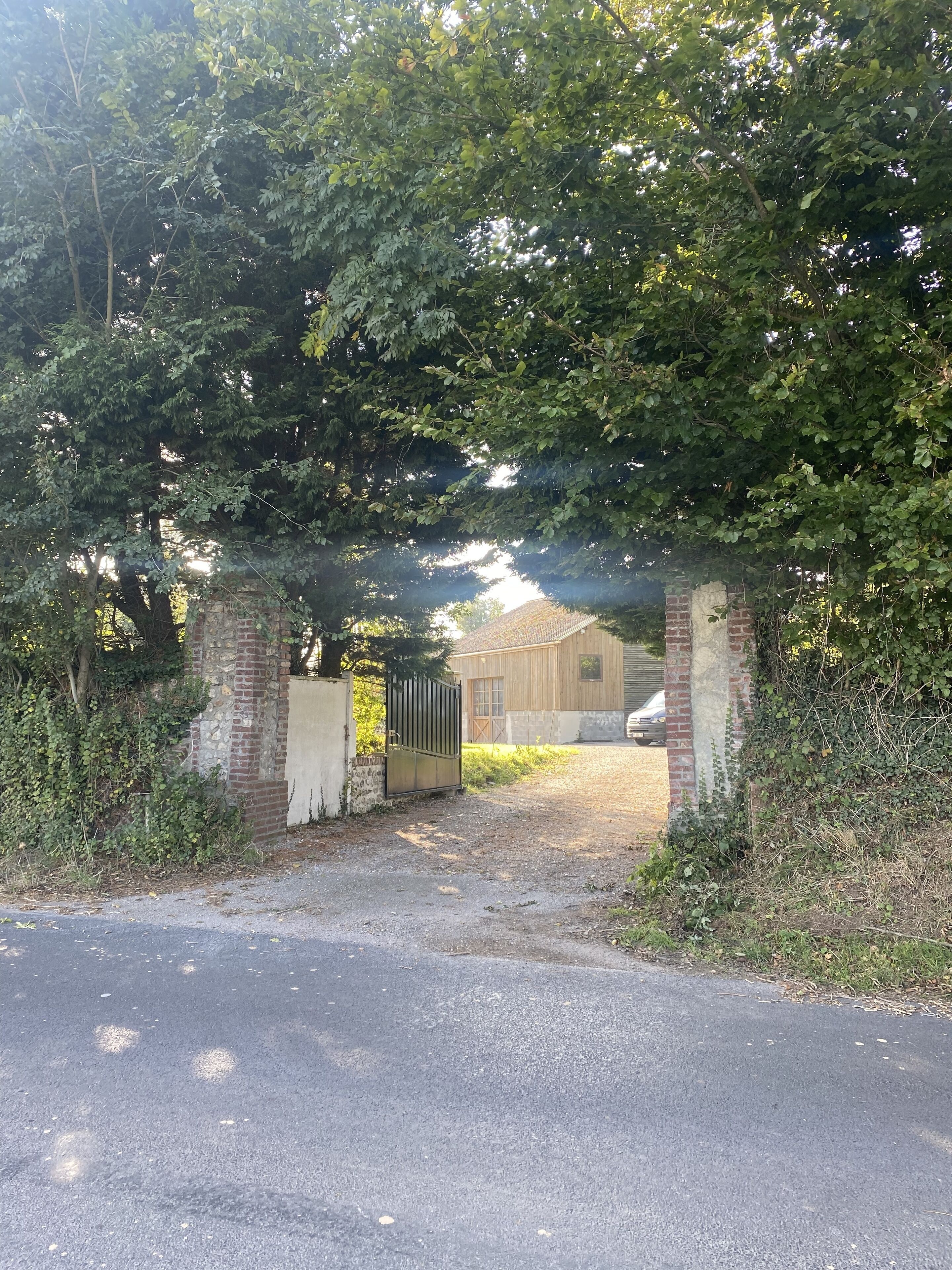 A gated entrance to a building with a brick wall and a metal gate, surrounded by dense foliage.