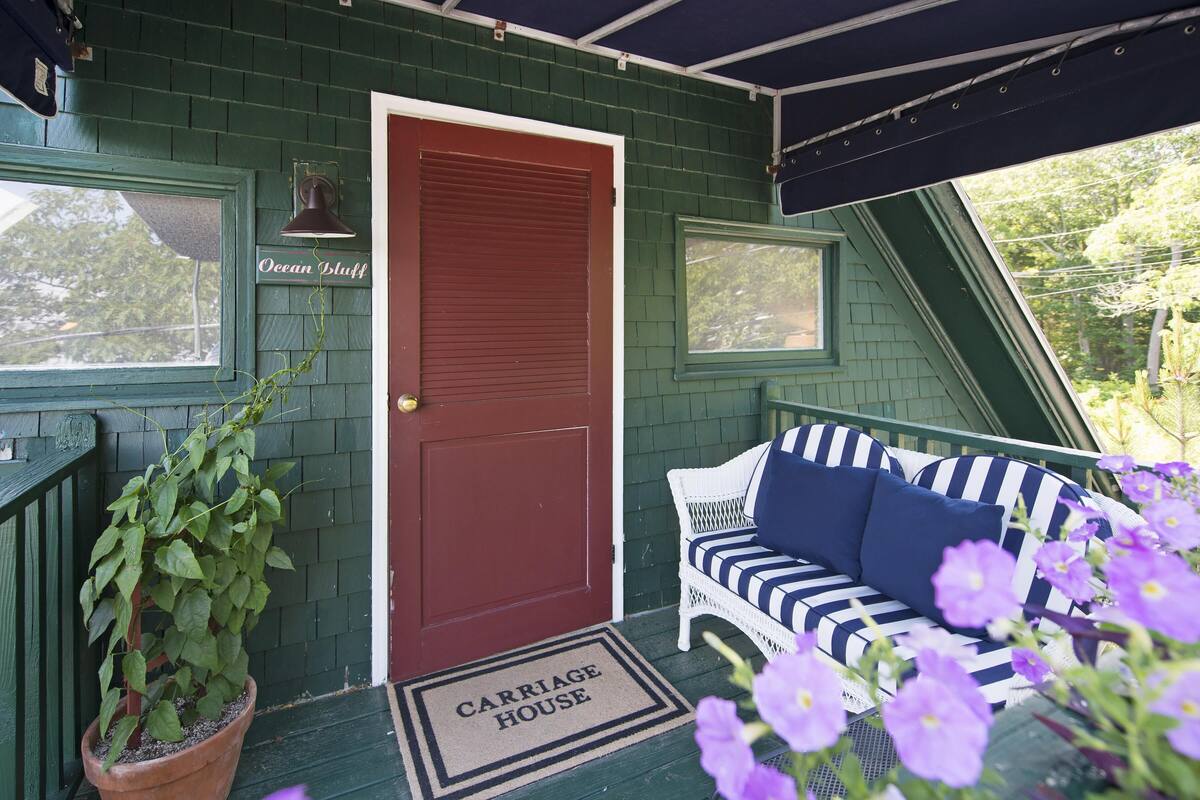 A green house with a red door, a porch with a striped sofa, and a potted plant.
