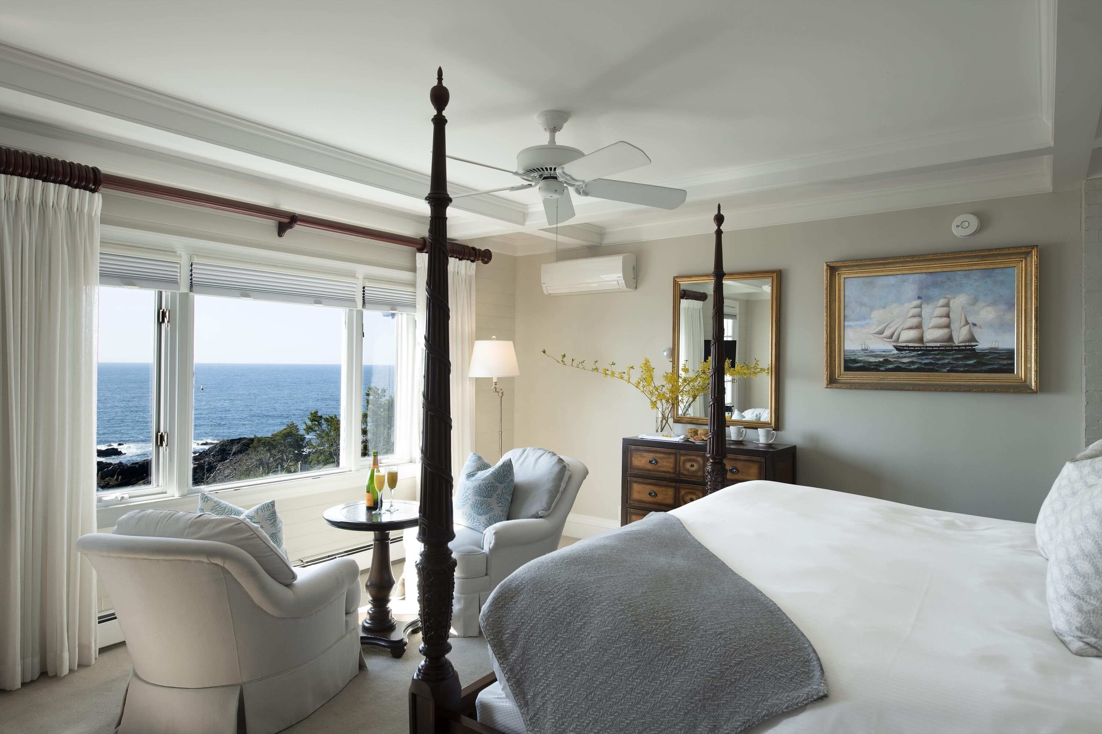 Quarto com cama de dossel, área de estar com uma poltrona, mesa com abajur e vista para o oceano.