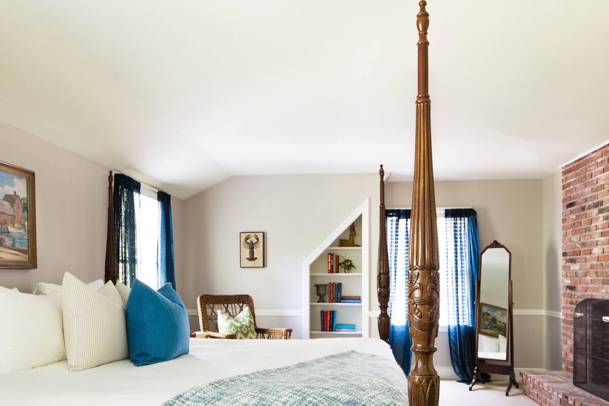 A bedroom with a four-poster bed, a bookshelf, a mirror, and a brick wall.