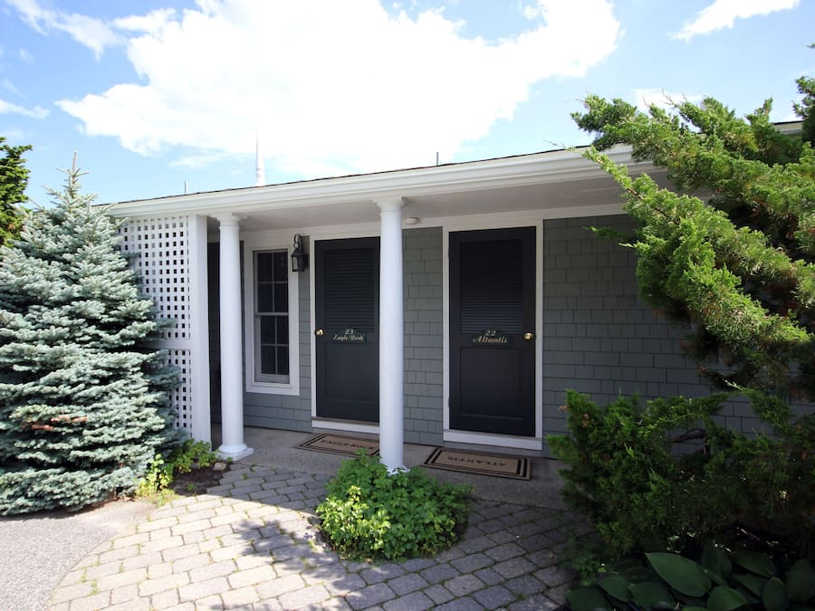 A building with a covered porch, two doors labeled "23" and "22," and a small garden area with a conifer and shrubs.