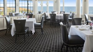 Comedor con mesas dispuestas para el servicio, amplias ventanas con vistas al mar y un suelo con diseño.
