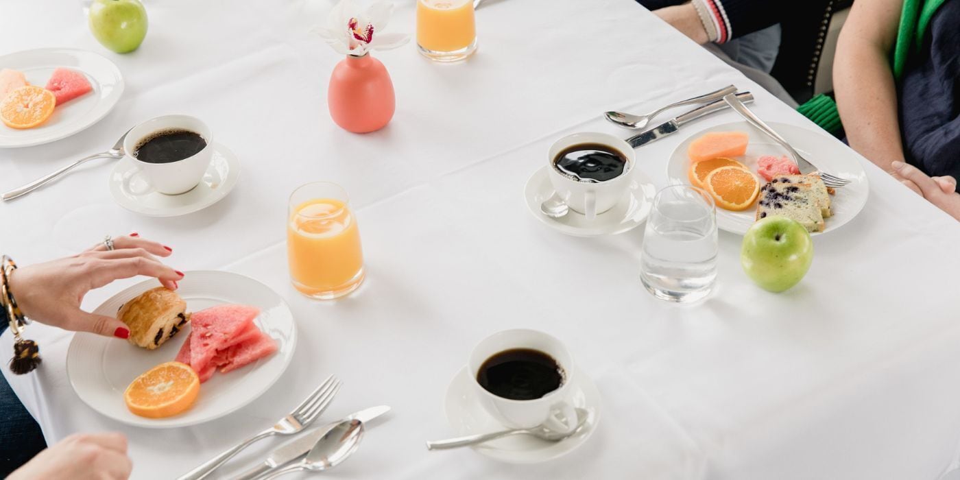 Ein Frühstückstisch mit Tellern voller Speisen, Kaffeetassen und einem Glas Orangensaft.