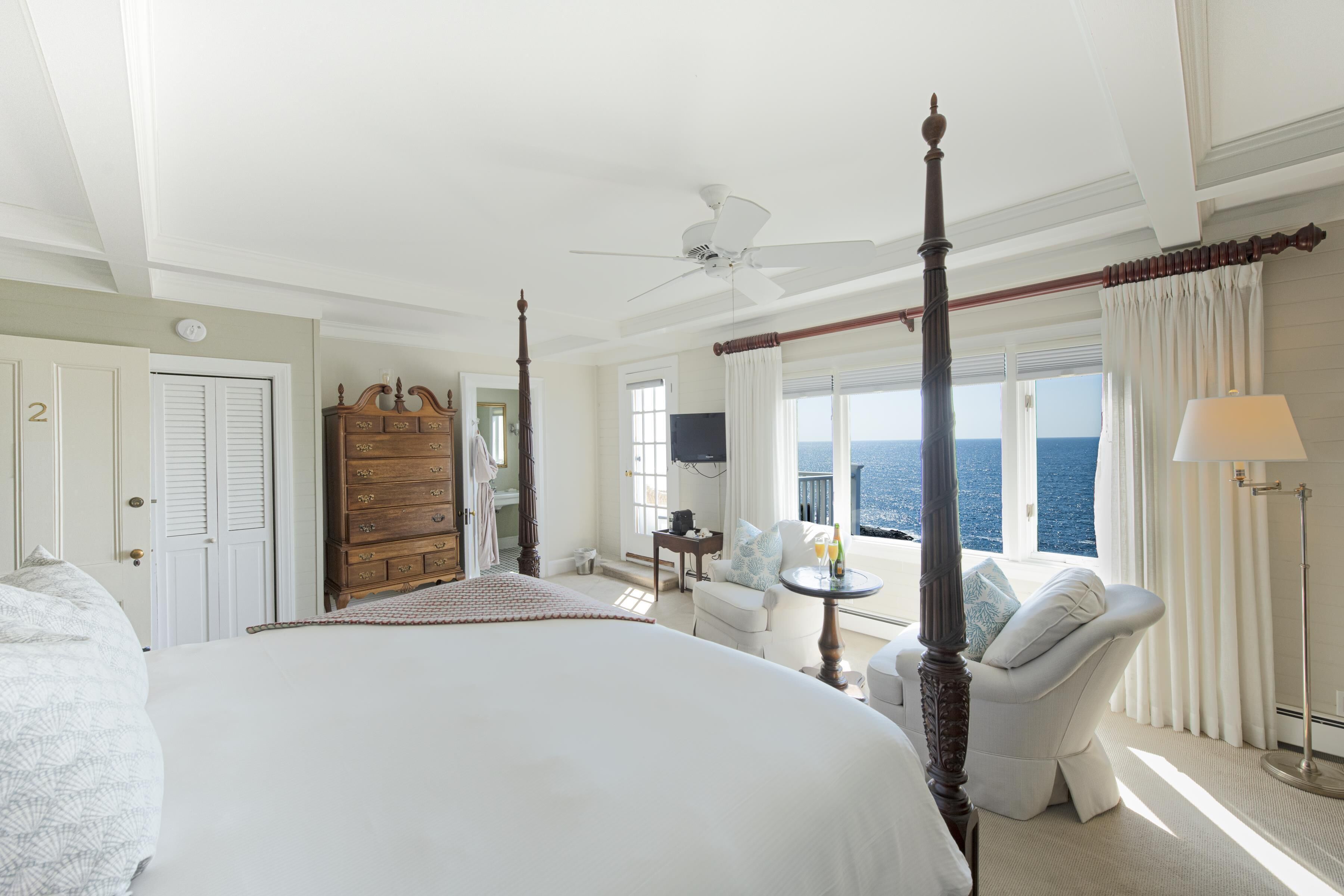 A spacious bedroom with a large bed, a four-poster bed, a sitting area with a view of the ocean, and a balcony with a view of the sea.