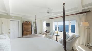A spacious bedroom with a large bed, a four-poster bed, a sitting area with a view of the ocean, and a balcony with a view of the sea.