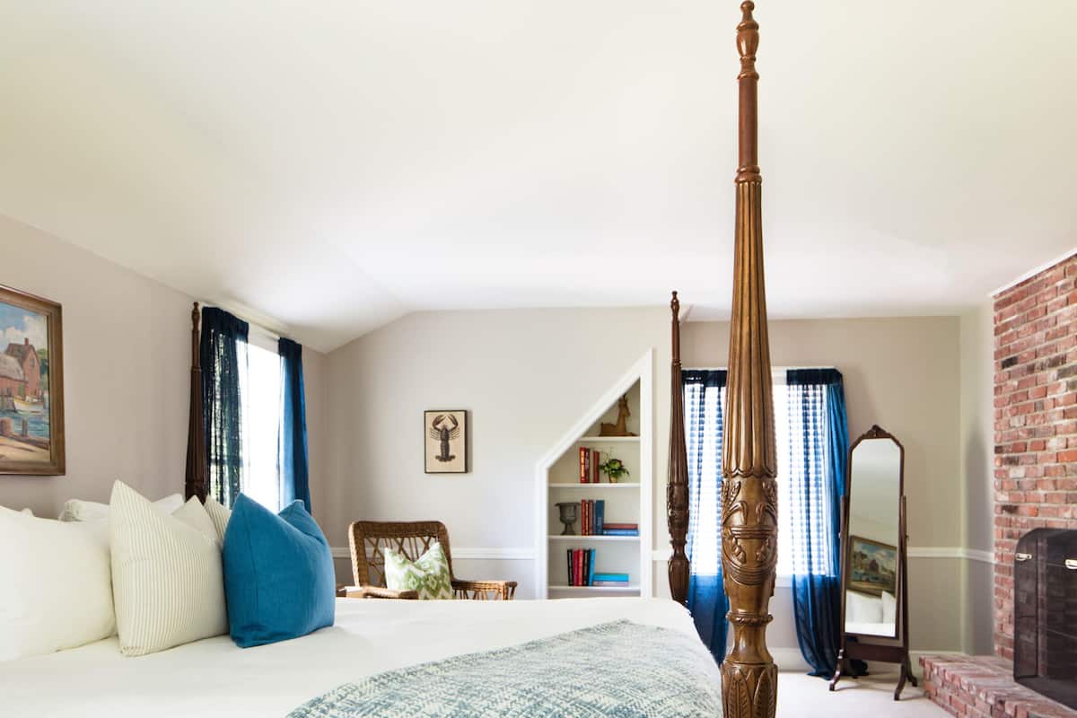 A bedroom with a four-poster bed, a bookshelf, a mirror, and a brick wall.