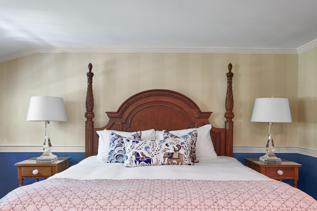 A neatly made bed with patterned pillows, a wooden headboard, and two bedside tables with lamps.