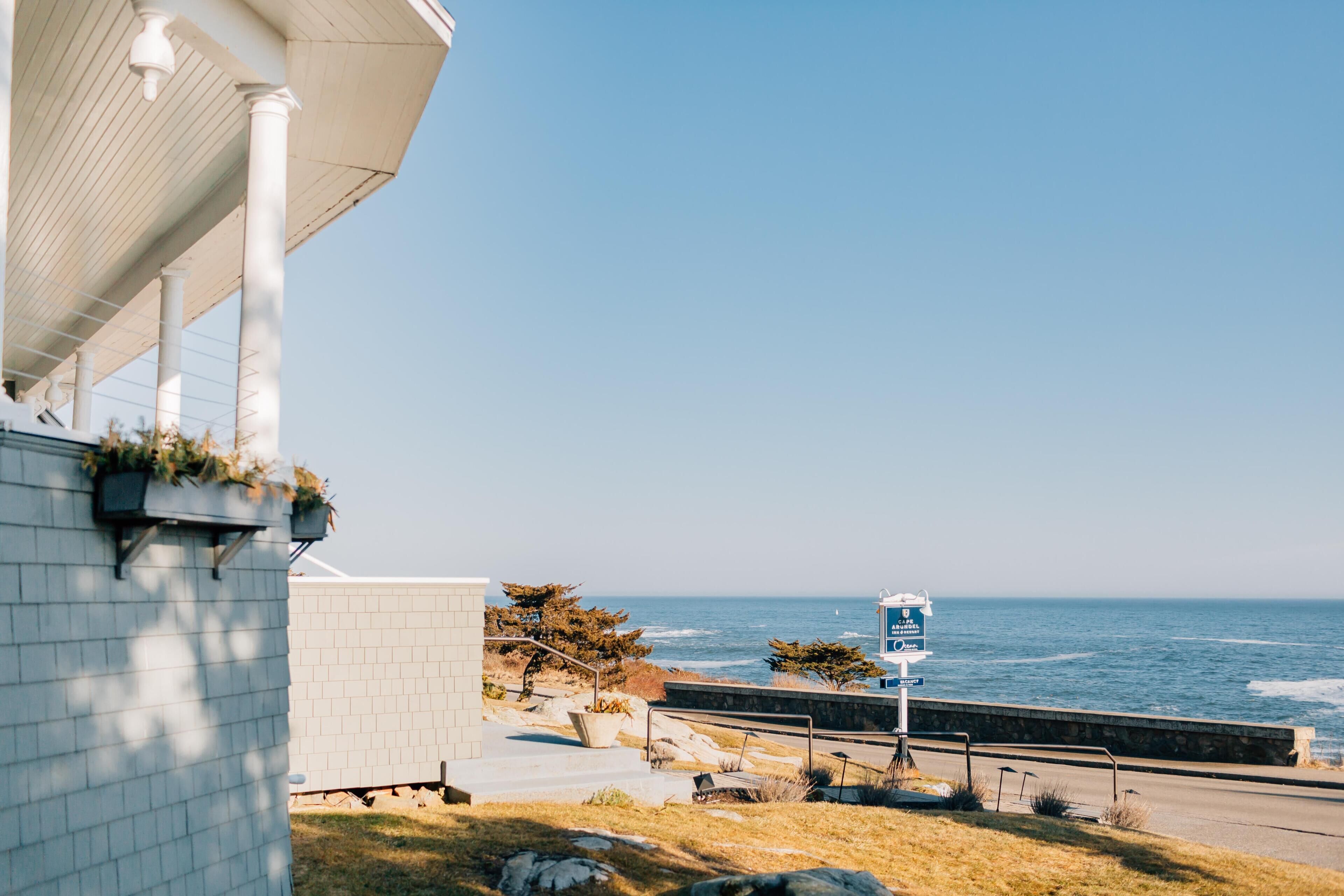 A coastal view with a white building, a paved walkway, and a sign indicating a marina.