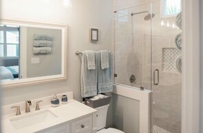 Un baño moderno con un espejo grande, dos lavamanos, una ducha con mampara de vidrio y toallas ordenadas.