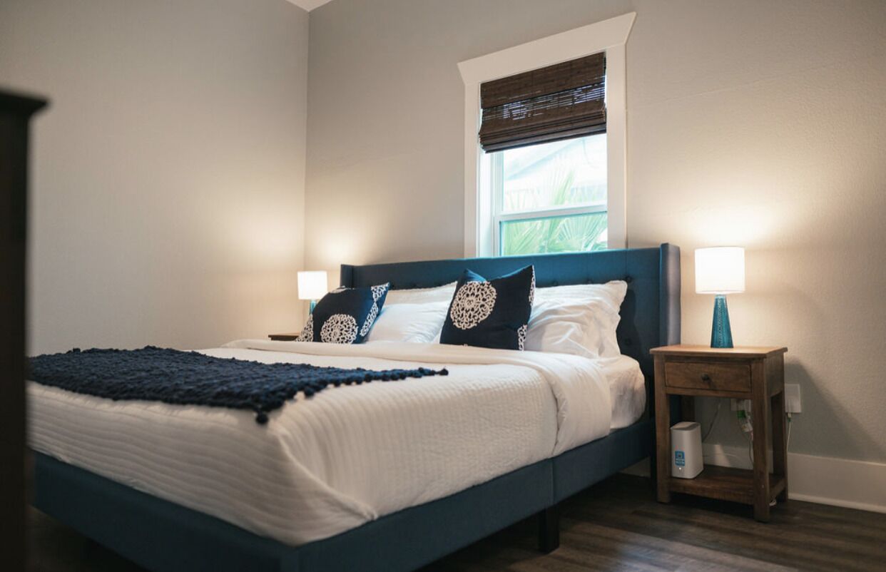 Un dormitorio con cama, dos lámparas de noche, una mesita de noche y una ventana con persianas.