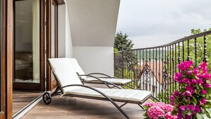 Een balkon met twee ligbedden, een glazen deur naar een kamer en uitzicht op een tuin met roze bloemen.