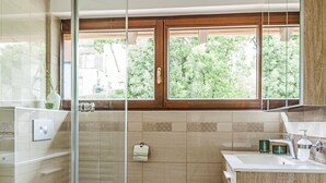 Een moderne badkamer met een glazen douchecabine, toilet, wastafel met spiegel en een raam voor natuurlijk licht.