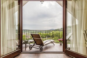 Een balkon met een stoel en tafel, met uitzicht op een tuin en heuvels in de verte.