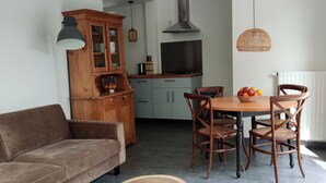 A cozy living room with a brown sofa, a wooden cabinet, and a dining area with a round table and chairs. - Beautiful detached house in an oasis of calm, close to beach and sea. (Koudekerke)