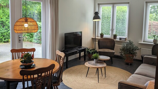 A spacious living room with a dining area, large windows, and a television. - Beautiful detached house in an oasis of calm, close to beach and sea. (Koudekerke)