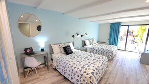 A bedroom with two beds, a desk, a chair, a round mirror, and a window with curtains.