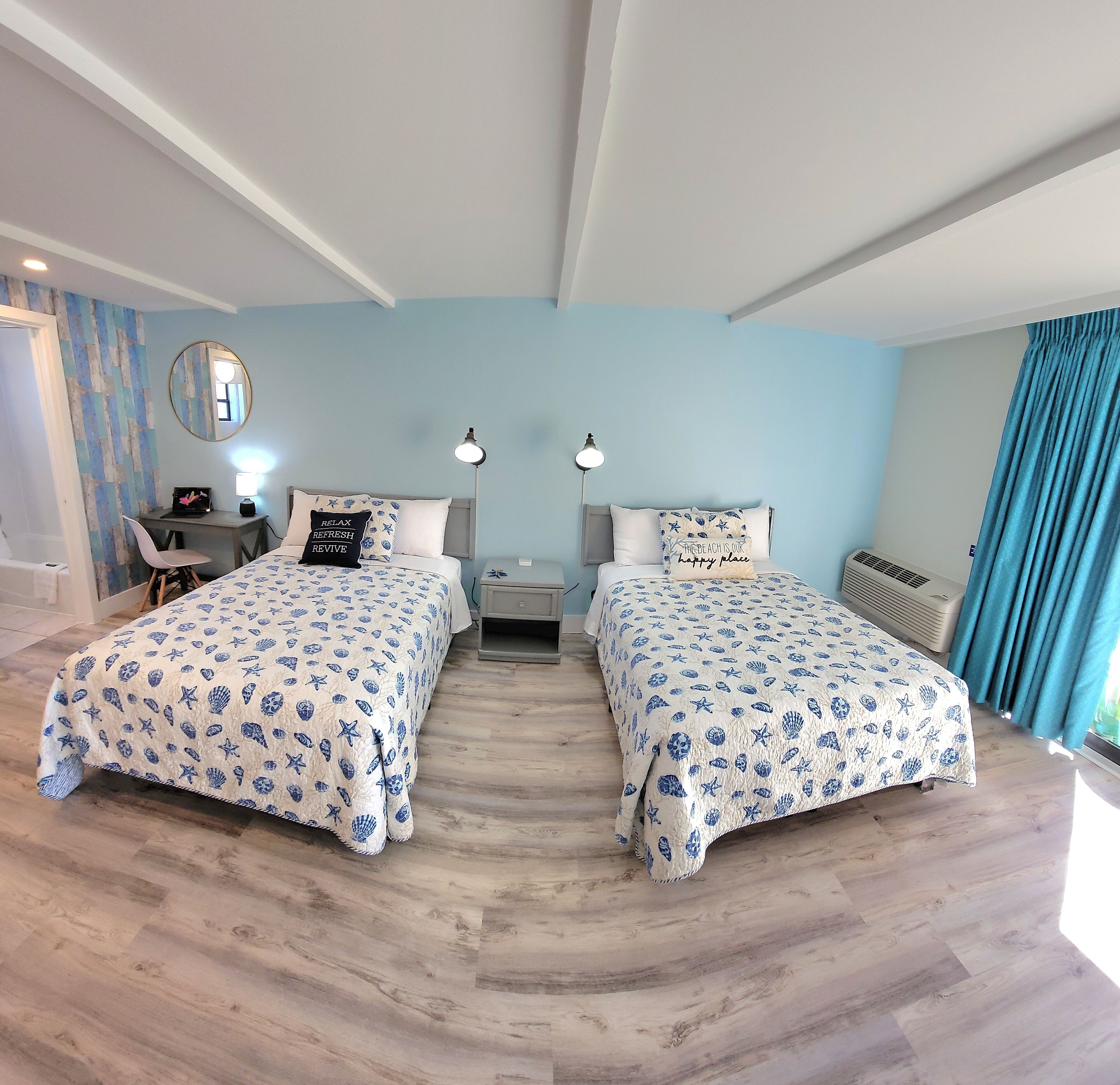 A room with two beds, a desk, a chair, a mirror, and a window with curtains.