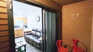 Ein Zimmer mit einer Schiebetür zu einer Küche, einem grauen Sofa und zwei roten Stühlen.