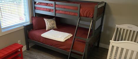 A bunk bed with red bedding and a ladder, a white crib, and a red bench.