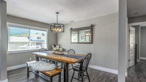 A dining area with a wooden table, black chairs, and a white bench. There is a chandelier above the table and a mirror on the wall. - Spacious 5BR with Sauna & AC, Fenced Yard,Fast WiFi, Near Willamette Pass (Oakridge)