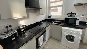 A compact kitchen with a stove, microwave, and washing machine. - Blackpool Abode - 124 Elite Apartments (Blackpool)