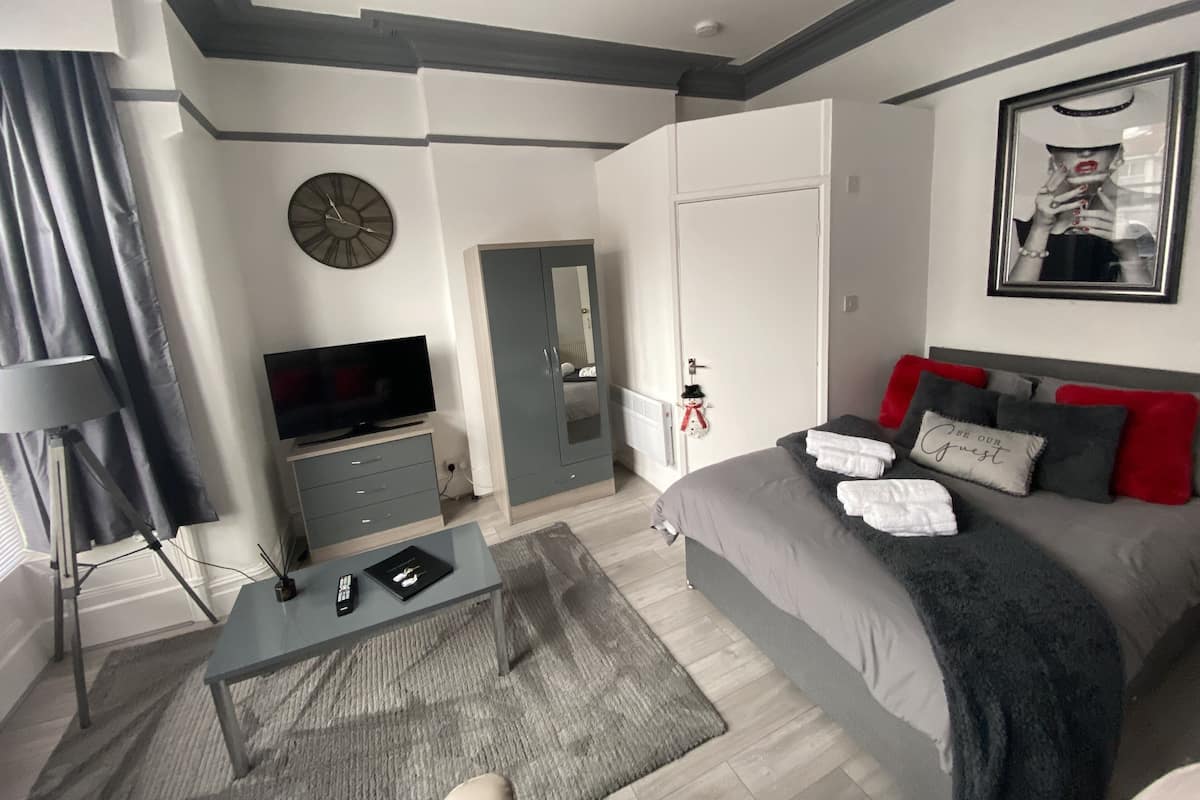 A modern bedroom with a bed, a television, a desk, and a mirror.