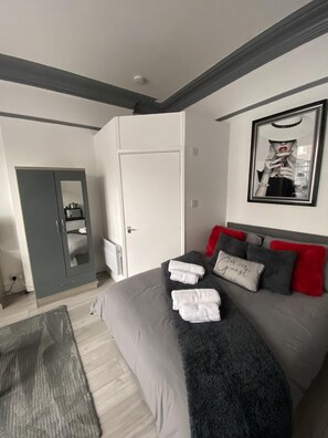 A modern bedroom with a grey bed, white towels, a grey wardrobe, and a framed picture on the wall. - Blackpool Abode - 124 Elite Apartments (Blackpool)