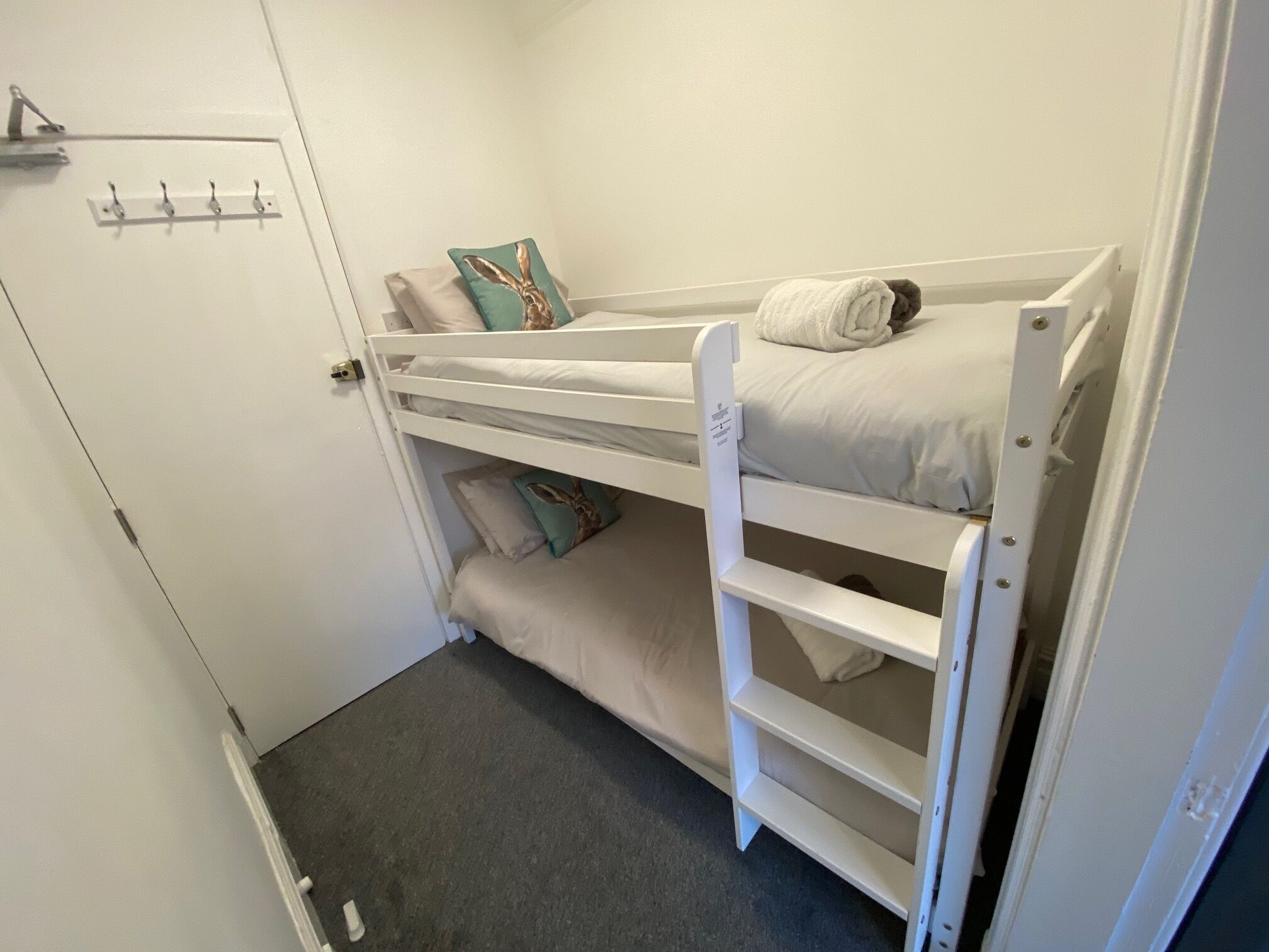 Una cama litera con un estante inferior, una puerta con cerradura y un panel de ganchos en la pared.