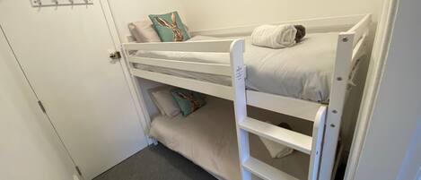 Una cama litera con un estante inferior, una puerta con cerradura y un panel de ganchos en la pared.