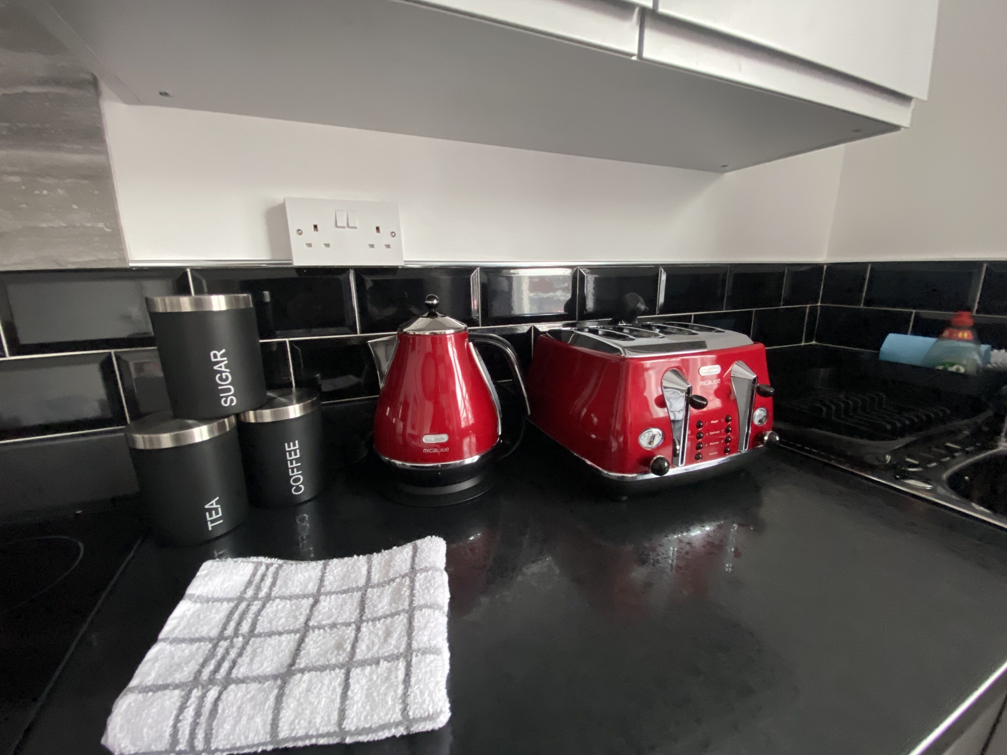 A kitchen counter with a coffee maker, sugar and tea containers, a red kettle, and a toaster.