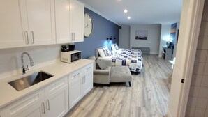A modern kitchen with white cabinets and a stainless steel sink. There is a microwave on the counter. The room has a blue accent wall and a large clock.