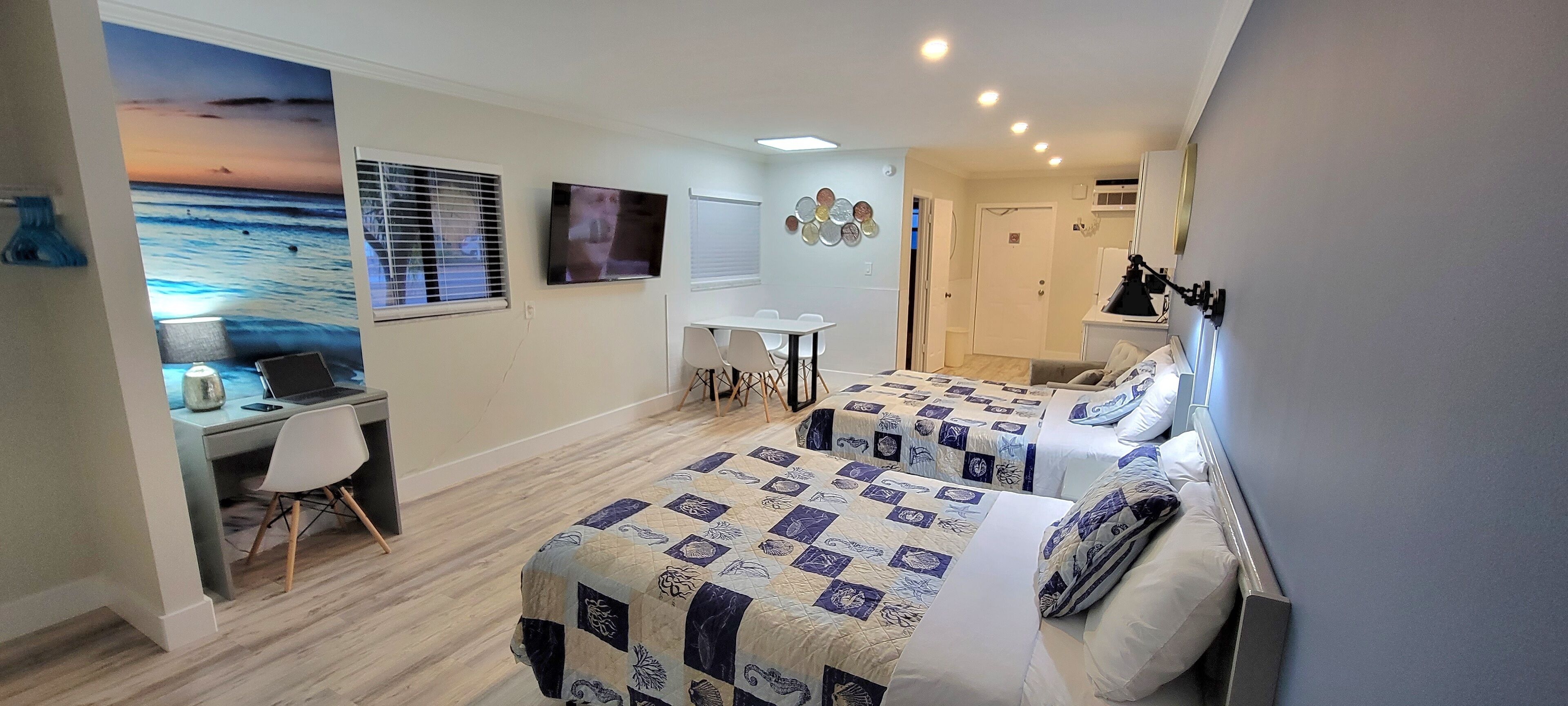 A hotel room with two beds, a desk, a TV, and a wall with a sunset mural.