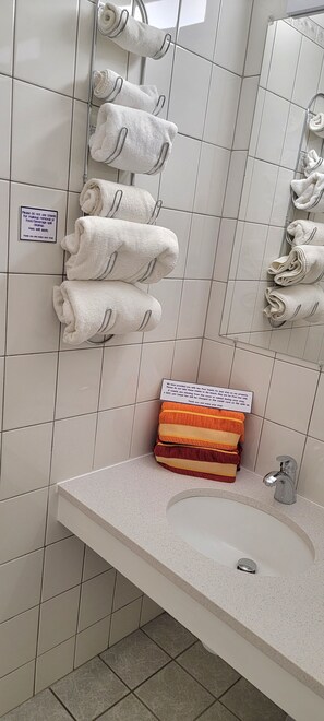 A bathroom with white tiled walls, a sink with a mirror, and towels hanging on a rack. - Satellite Motel - Vacation Station 126 (Treasure Island)