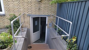 A set of outdoor wooden steps leading to a door, flanked by metal handrails and potted plants.