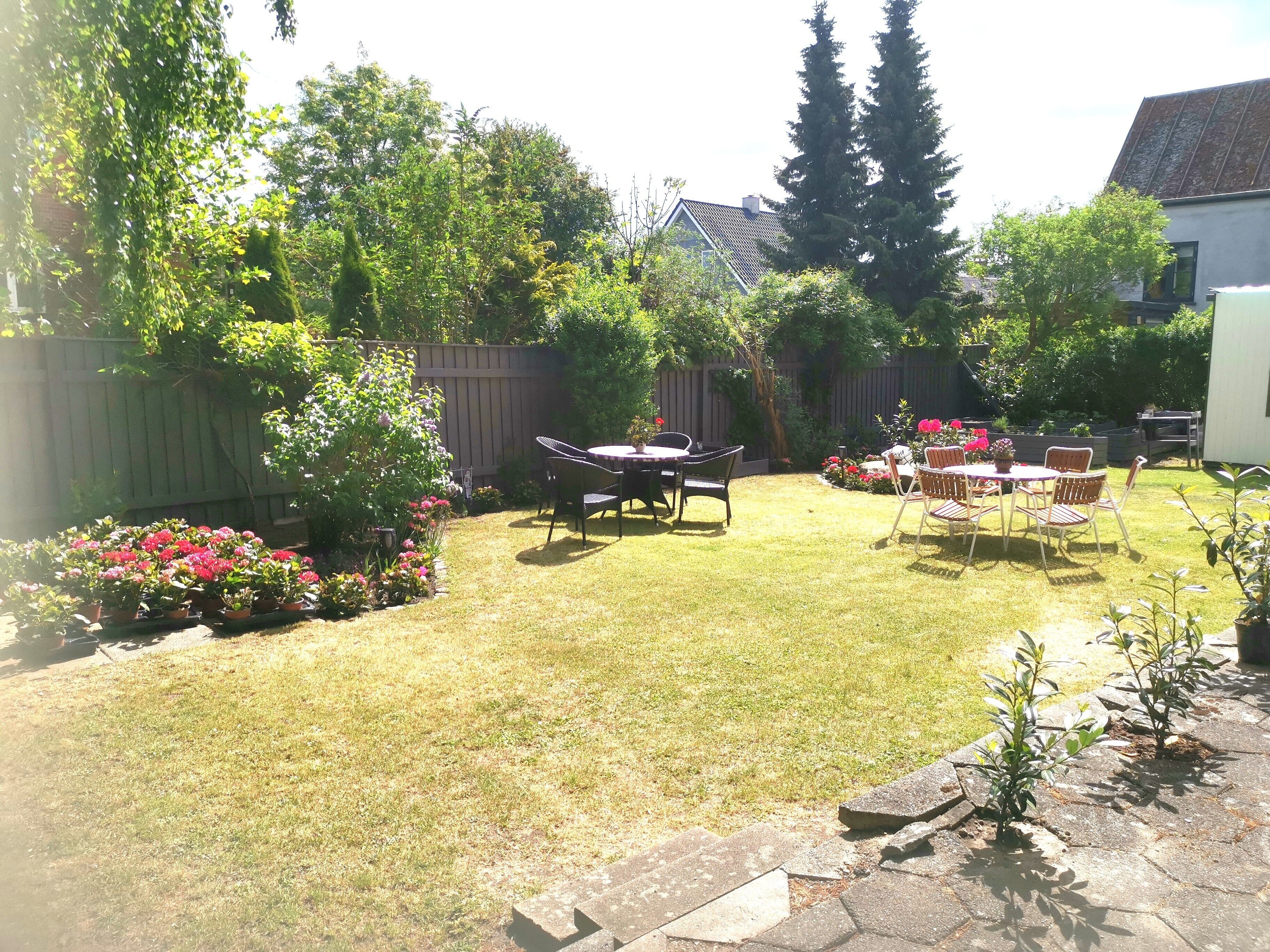 Un jardin avec une pelouse, une clôture en bois et un espace patio aménagé avec des chaises et une table.