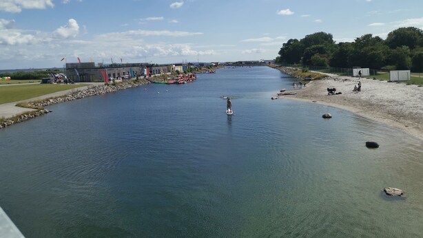 A river with a pier, boats, and a building with flags.