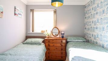 Une chambre avec deux lits simples, une commode, un miroir, une fenêtre et un mur décoré d’un motif.