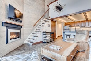 A modern living room with a fireplace, a wooden coffee table, a comfortable armchair, and a staircase leading to an upper level.