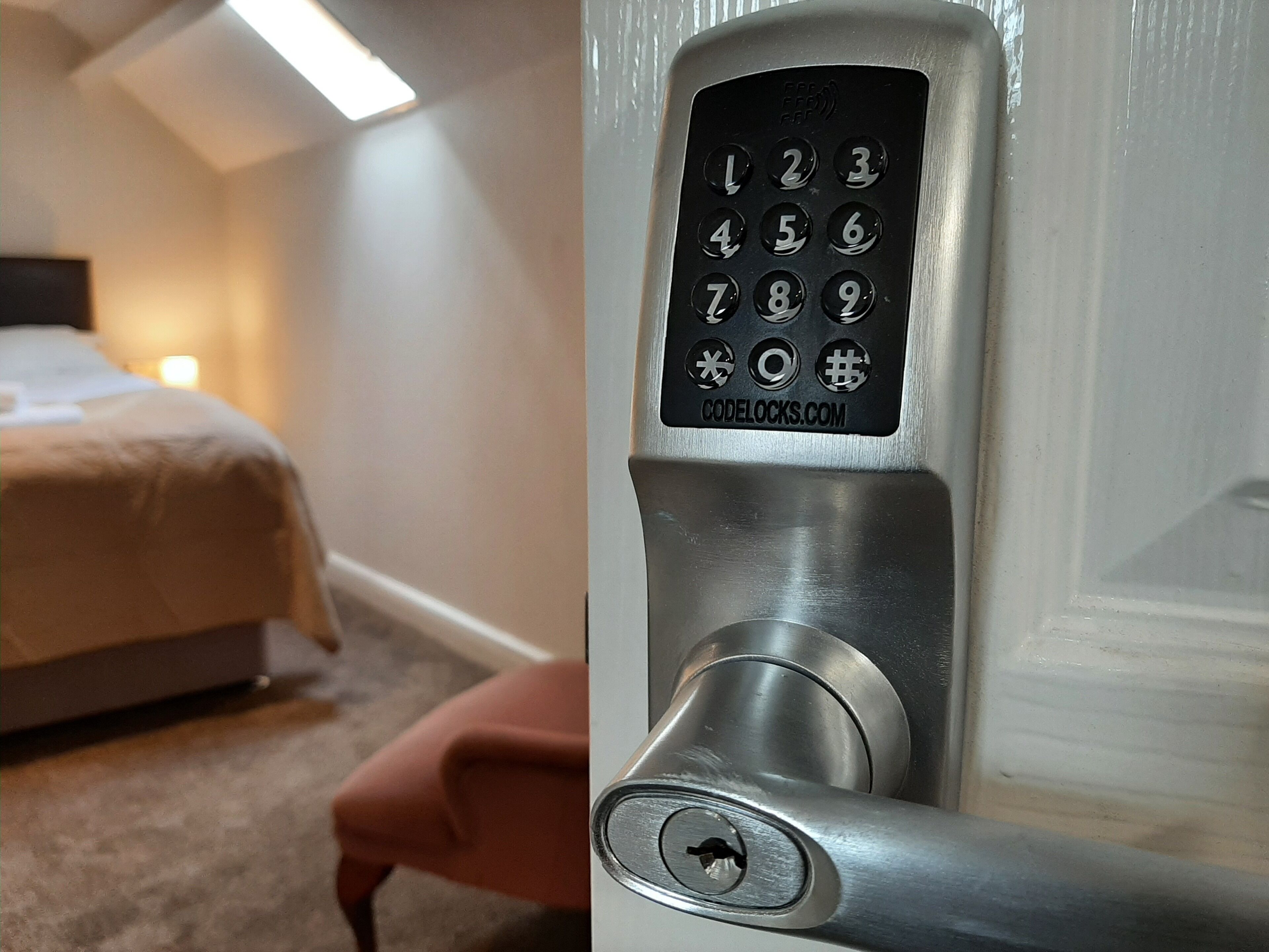 A hotel room with a bed, a nightstand, and a door with a numeric keypad lock.