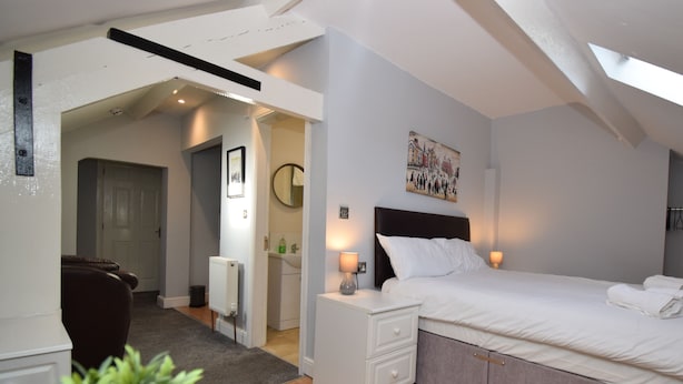 A bedroom with a bed, bedside tables, a nightstand, a radiator, a mirror, and a painting on the wall. - Malton Central Apartments (Malton)