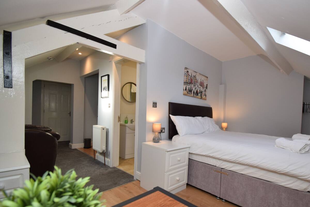 A bedroom with a bed, bedside tables, a nightstand, a radiator, a mirror, and a painting on the wall.