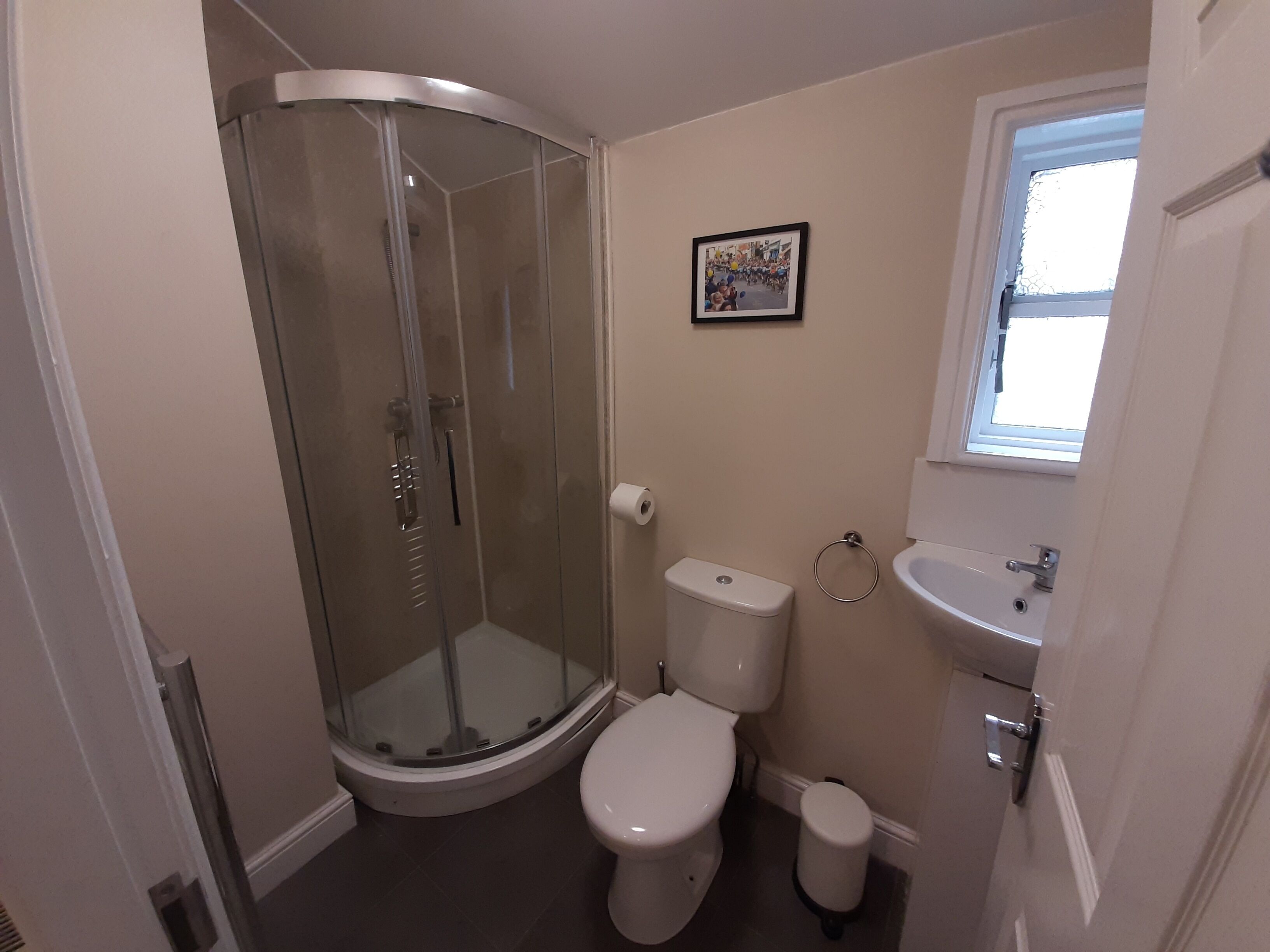A bathroom with a glass-enclosed shower, a toilet, a sink, and a small window.