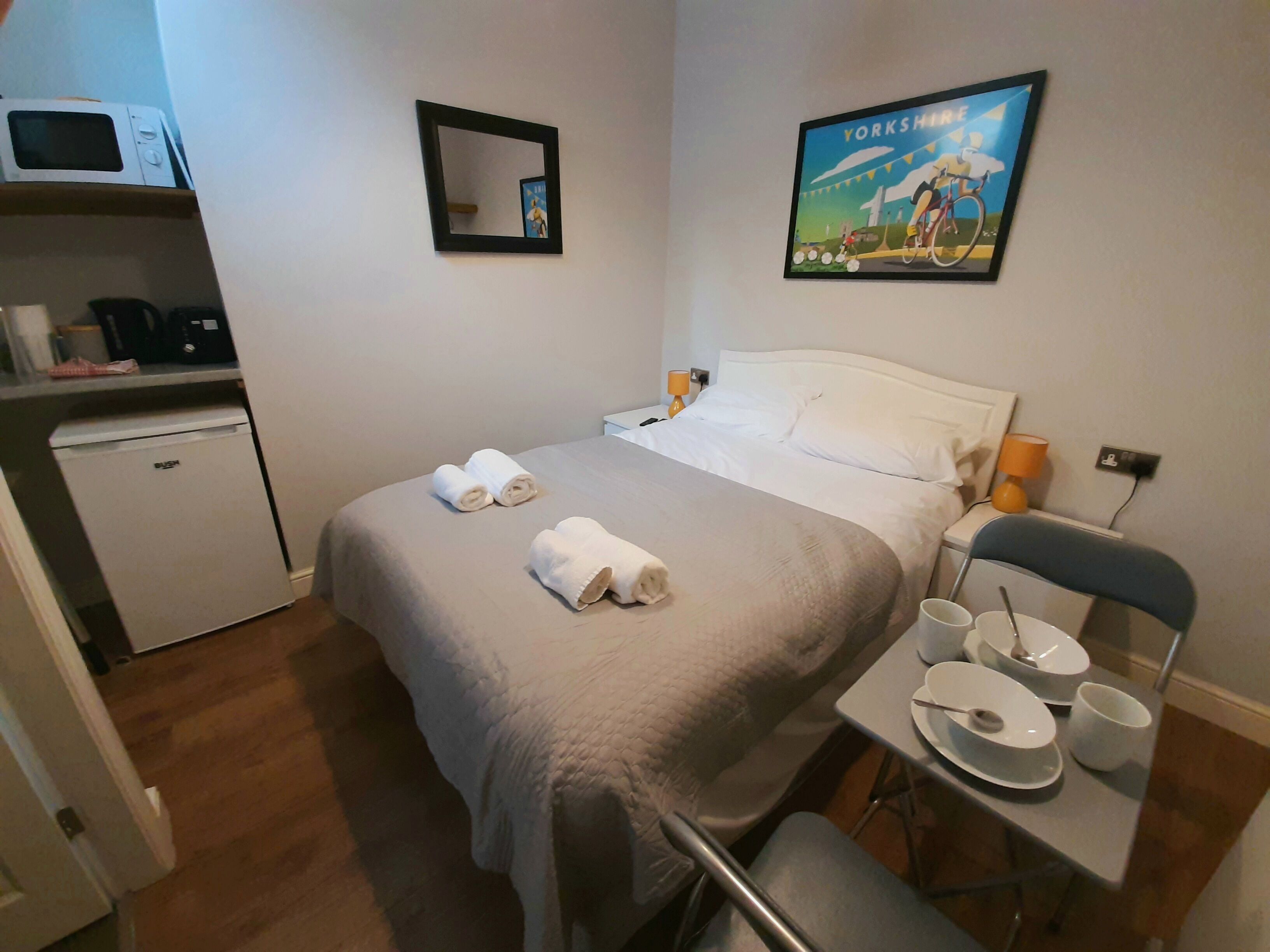 Ett hotellrum med en säng, ett litet skrivbord med en stol, en mikrovågsugn, ett minikylskåp, en spegel och en inramad tavla på väggen.