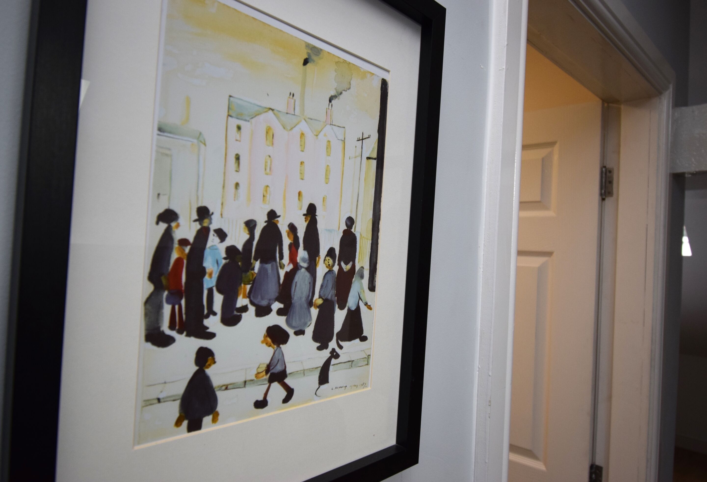 A framed artwork depicting a group of people in a street scene.