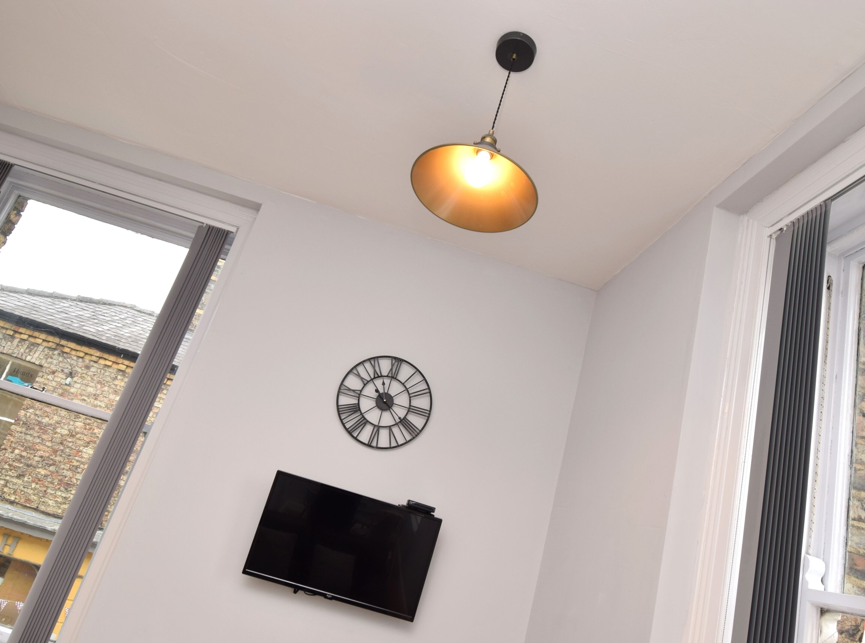 A room with a wall-mounted clock, a flat-screen TV, and a pendant light.