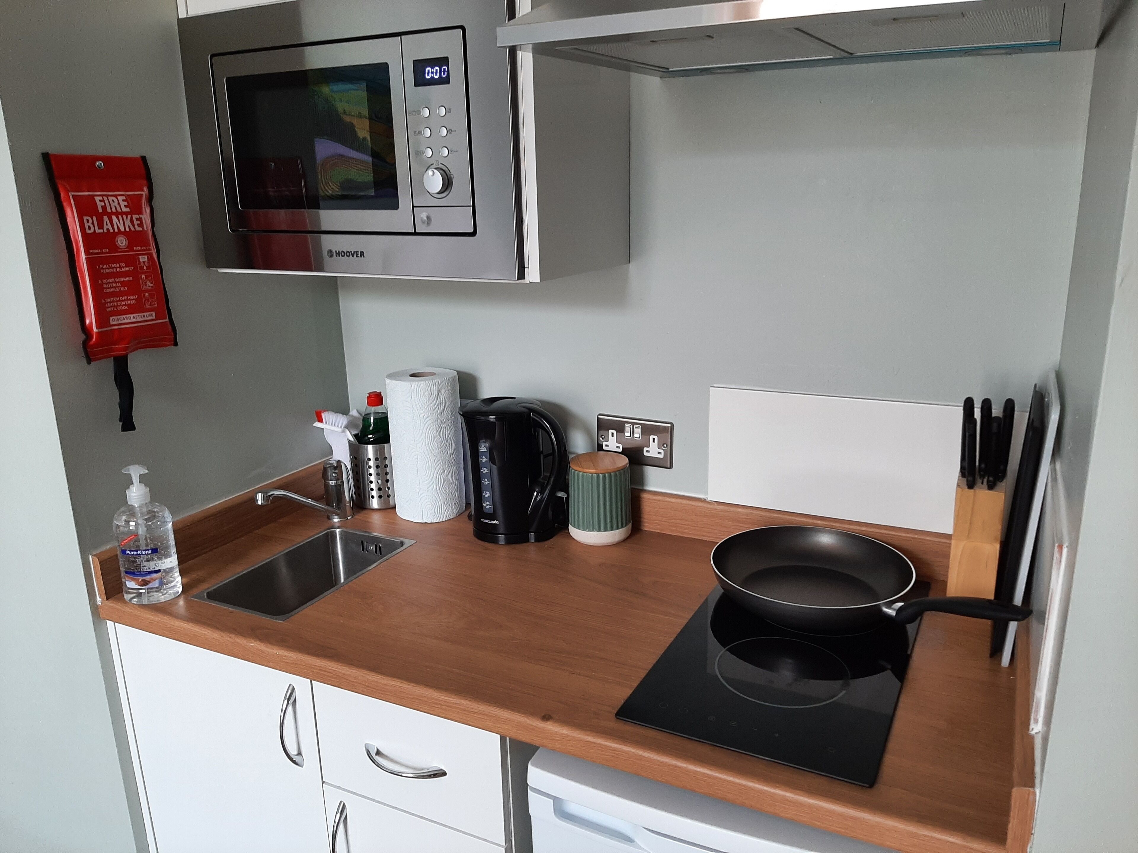 A compact kitchen with a microwave, kettle, and induction cooktop.