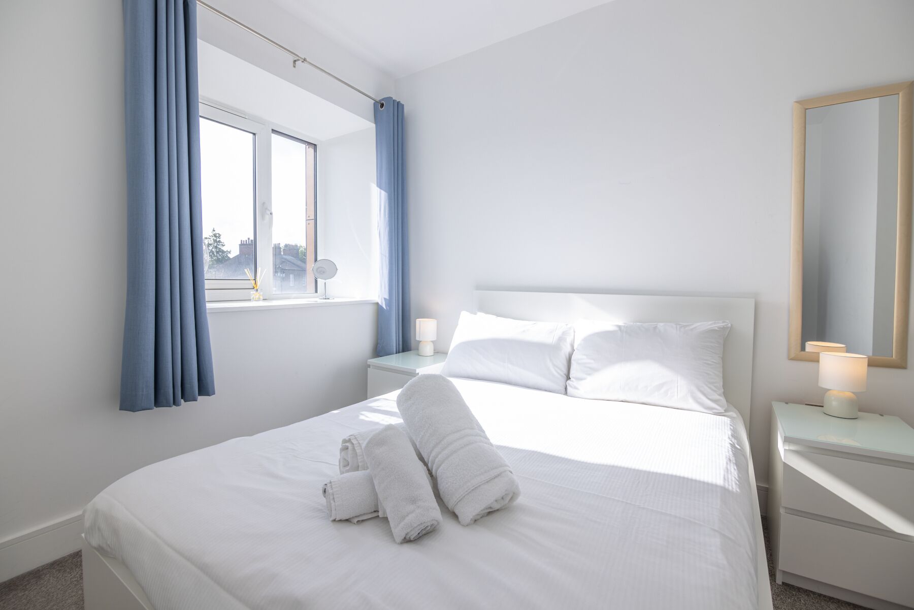 Una habitación de hotel con cama, mesita de noche, lámpara y ventana con cortinas.
