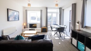 Un salon moderne comprenant un canapé, un téléviseur, une table à manger avec des chaises et une grande fenêtre avec des rideaux.