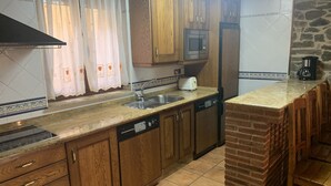 A kitchen with wooden cabinets, a built-in microwave, a dishwasher, and a brick accent wall. - Casa Rural (La Horcajada)