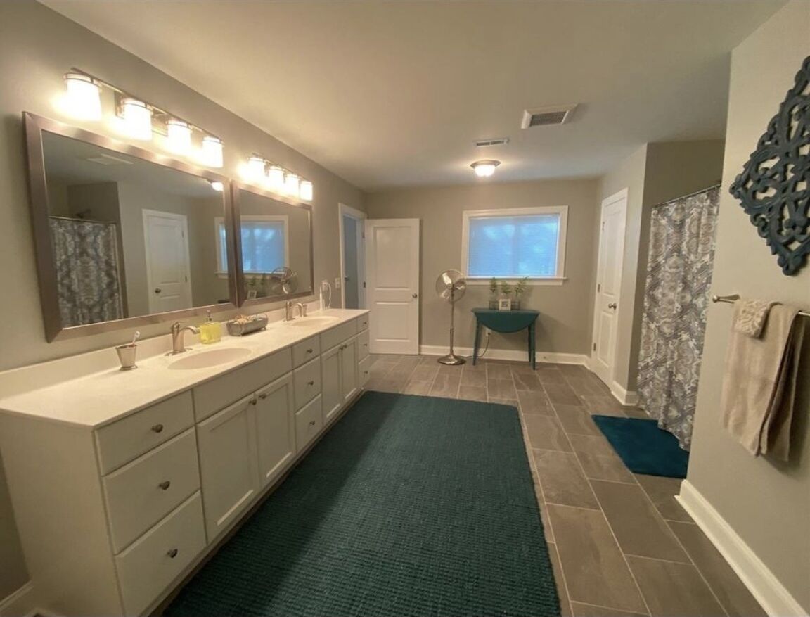 A bathroom with a large vanity, a mirror with lights, a window, and a shower area.